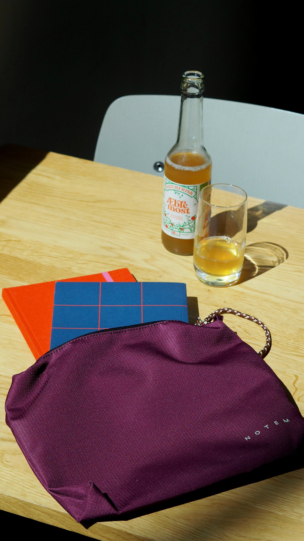Purple clutch bag on a wooden table with a bottle and glass of beer.